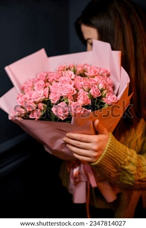 Young darkhair woman florist holding in hands large bouquet of fresh pink roses wrapped in pink paper and decorated with satin ribbon Royalty-Free Stock Photo #2347814027