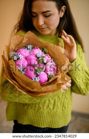 Young beautiful darkhair woman in green sweater posing with luxury bouquet of fresh pink peonies and blue small decorative flowers in stairwell interior Royalty-Free Stock Photo #2347814029