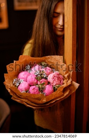 Young beautiful darkhair woman posing with luxury bouquet of fresh pink peonies and small decorative flowers near wooden doors Royalty-Free Stock Photo #2347814069