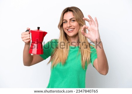 Young Uruguayan woman holding coffee pot isolated on white background showing ok sign with fingers