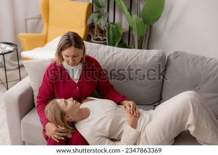 Lifestyle psychologist, cheerful elderly parent mom provides psychological support to an young adult daughter woman in room house. Family day concept.