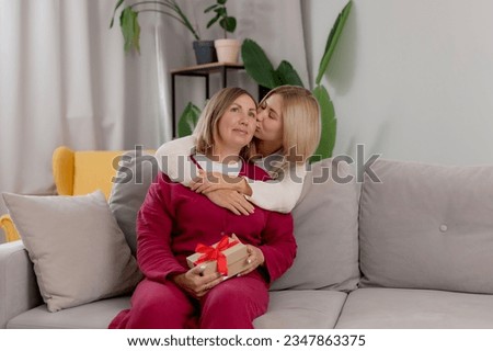 Loving young adult woman child congratulate excited elderly mother with birthday or mom day anniversary at living home. Smiling caring grownup daughter present gift to old lady.