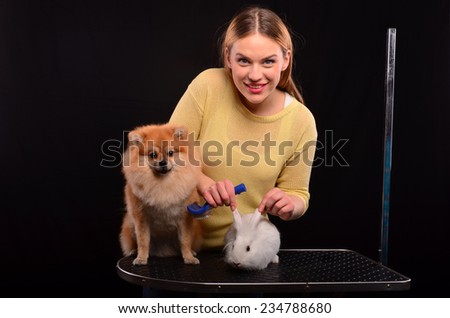Young, beautiful blonde girl grooming Pomeranian dog and white bunny