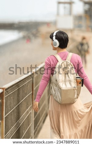 Student walking along the boardwalk listening to music, wearing headphones and carrying a backpack.