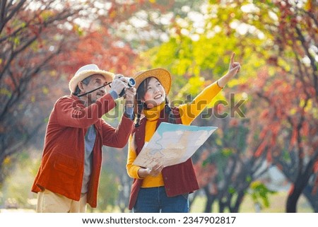 Happy Asian daughter and her senior father are walking together in public park during autumn with maple and ginkgo tree while using map for fall color travel destination and family happiness