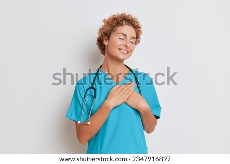 Doctor young curly woman smiling gently with closed eyes, hands pressed to her heart, picture set on white background, good doctor concept, copy space