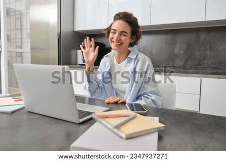 Happy young woman, tutor teacher students online. Girl connects to remote work meeting from her home laptop, says hello, waves hand at computer.