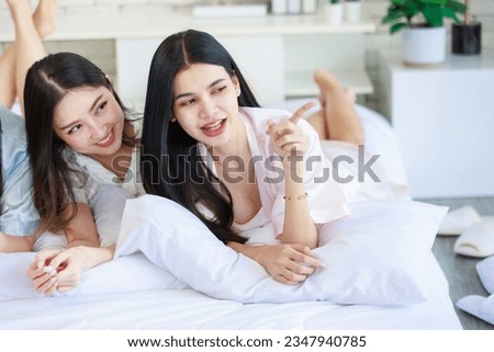 Closeup Asian beautiful cheerful happy female girlfriends in casual pajamas outfit laying lying down on pillows smiling talking having conversation slumber party together at night on bed in bedroom. Royalty-Free Stock Photo #2347940785