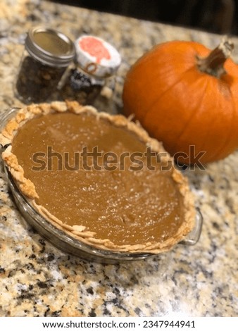 Pumpkin pie, orange pumpkin and pumpkin seeds in jars sitting on counter top