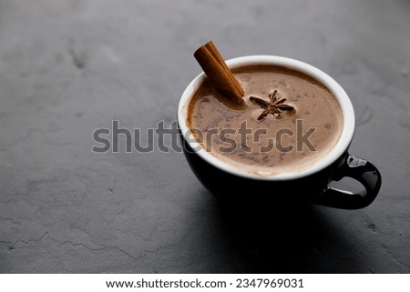 Spicy hot chocolate with cinnamon in ceramic blue cup on dark stone background.