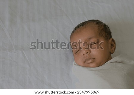 Closeup picture of an Indian new born baby boy swaddled in white cloth sleeping peacefully on a white bedsheet. Peaceful, eyes, cute, nap, rest, kid, innocence, love, care, affection, asian, health