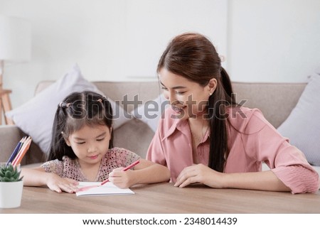 Educational pastime develop creativity skill in kid concept. Asian mother her small daughter in sunny cozy living room, mom teach girl paint use paper and colourful pencils