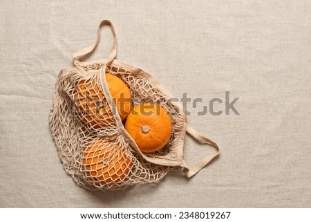 Pumpkins in a string bag on a beige textile background. Top view, flat lay