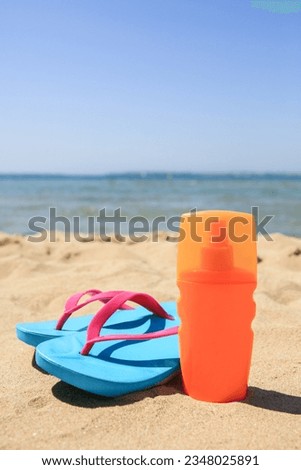 Sunscreen and flip flops on sandy beach. Sun protection care