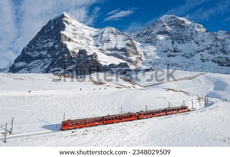 A cogwheel train travels on the railway from Jungfraujoch (top of Europe) to Kleine Scheidegg on the snowy hillside with Eiger, Monch and Jungfrau in background in Bernese Highlands, Switzerland Royalty-Free Stock Photo #2348029509