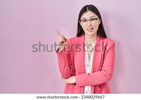 Chinese business young woman wearing glasses with a big smile on face, pointing with hand and finger to the side looking at the camera. 