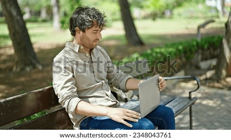Young hispanic man using laptop sitting on bench at park