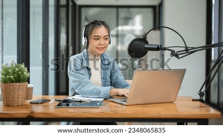 A beautiful Asian female podcaster or radio host working in her studio, speaking into a microphone, recording her podcast.
