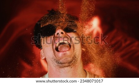 Brave man sprinkles himself with sparkle particles. Glamour luxury photo, shine face, open mouth. Rich view portrait male person in sunglasses, pouring on face gold glitter