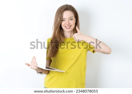 young beautiful blonde woman wearing yellow T-shirt over white directing empty space  hold laptop