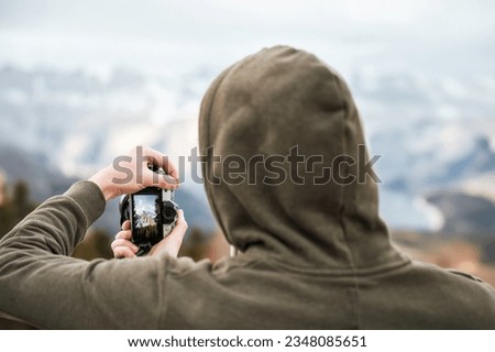 Close-up of a man holding a modern photo camera while looking at the screen. Using a Camera with the screen visible. Concept of an amateur taking photos in the mountains.