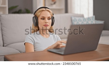 Young blonde woman using laptop and headphones sitting on floor at home