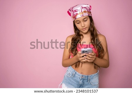 Photo portrait of little child girl with long brunette hair dreaming smiling keeping smartphone isolated on pink color background