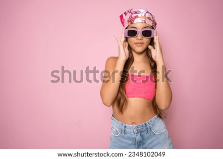 Portrait of cute child girl wearing sunglasses in summer clothing standing isolated over pink background.