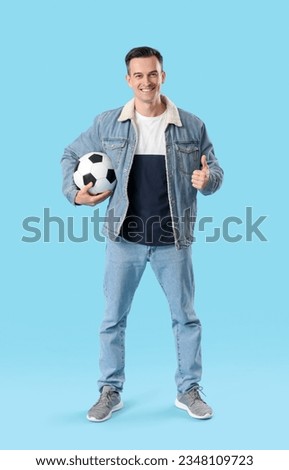 Young man with soccer ball showing thumb-up on blue background
