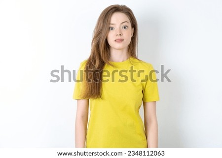 Stunned young beautiful blonde woman wearing yellow T-shirt over white stares reacts on shocking news. Astonished girl holds breath