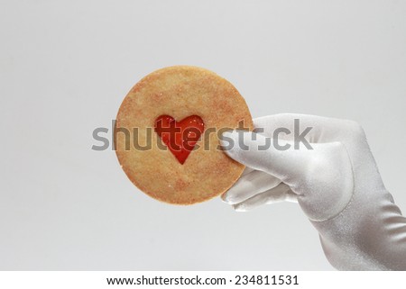 White elegant female gloves holding a cookie with heart-shaped lam isolated on white background