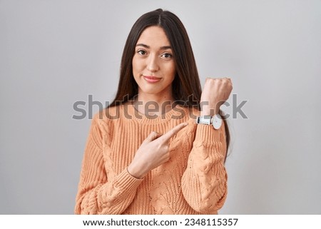 Young brunette woman standing over white background in hurry pointing to watch time, impatience, looking at the camera with relaxed expression  Royalty-Free Stock Photo #2348115357
