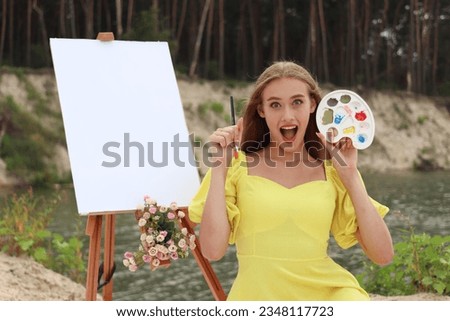 Portrait of creative woman artist sitting working on a new idea painting in nature. She is drawing with paints, pencils, palette and a brush. She is sitting near the easel. She is shocking
