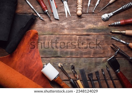 Leather pieces and leather craft work tools on the old wooden workbench background. Royalty-Free Stock Photo #2348124029
