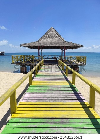Wooden pier with attractive colors on Gili Genting Beach, Madura, Indonesia. Traditional fishing boats with colorful patterns anchored on the beach. Minimalistic photo of the sea, a boat and the sky.
