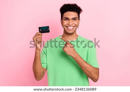 Photo of cheerful positive guy wear green t-shirt pointing finger bank card isolated pink color background