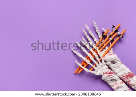 Skeleton hands with straws for Halloween celebration on purple background