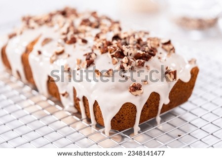 Glazing pumpkin bread with a white glaze and garnishing with shopped pecans. Royalty-Free Stock Photo #2348141477