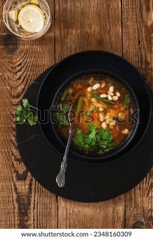 Minestrone soup with seasonal summer vegetables, healthy vegan meal in black plate on wooden table, directly above