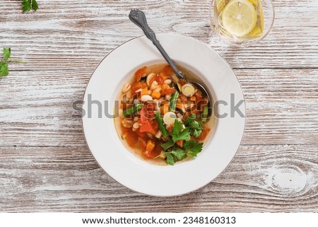 Minestrone soup with seasonal summer vegetables, healthy vegan meal in rustic plate on wooden table, high angle view