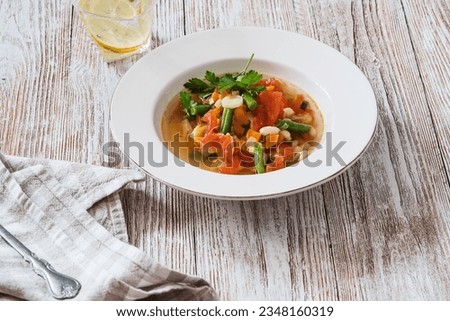 Minestrone soup with seasonal summer vegetables, healthy vegan meal in rustic plate on wooden table