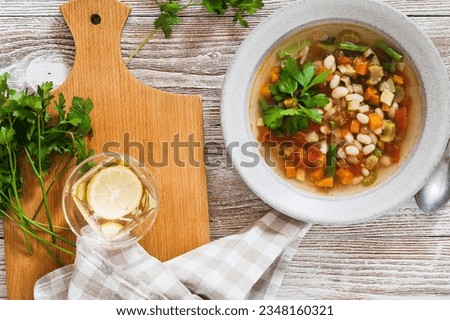 Minestrone soup with seasonal summer vegetables, healthy vegan meal in rustic plate on wooden table, high angle view