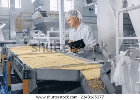 Concept modern food industry, factory production line. Worker man control quality product on automatic conveyor belt for transporting cedar nuts.
