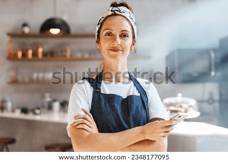 Caucasian coffee shop owner standing in her establishment, embracing technology with her smartphone and using it to streamline operations and provide a modern, efficient experience for her customers. Royalty-Free Stock Photo #2348177095