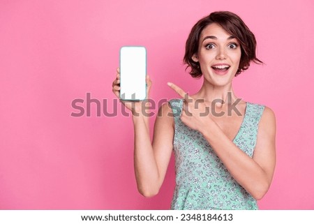 Photo of young woman directing finger empty space smartphone touchscreen surprised website app store isolated on pink color background