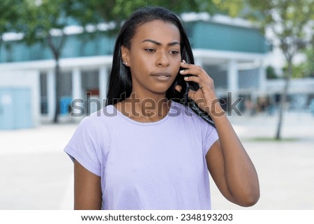 Concerned and serious latin american woman listening at phone outdoor in summer in city Royalty-Free Stock Photo #2348193203