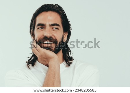 Handsome young man smiling in a studio, proudly wearing his beautiful beard and long hair, as well as his glowing and youthful skin. Happy caucasian male embracing grooming and self-care. Royalty-Free Stock Photo #2348205585