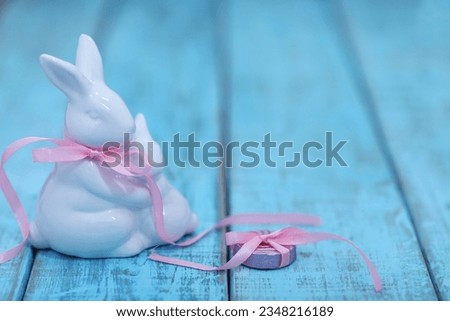 White ceramic bunny with pink ribbon, on blue background, holiday, greeting, free space, place for text, background image