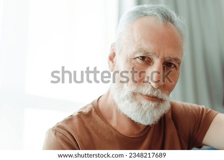 Portrait of attractive smiling senior man with beard in brown t shirt looking at camera, closeup. Handsome male model posing for picture. Concept of advertisement, customer service
