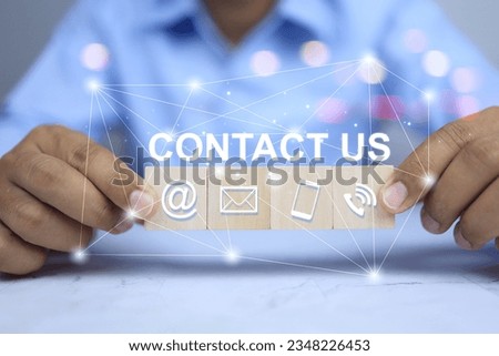 Contact us concept. Businessman holding wooden block with contact us word e mail social media chanel smart phone icon. Products information customer inquiry.